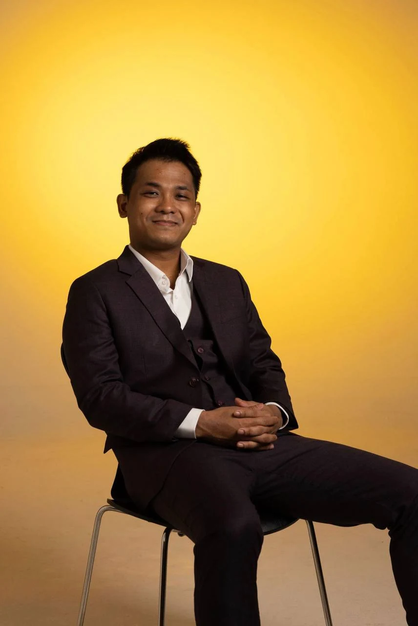 Zin, seated in a suit against a warm golden background